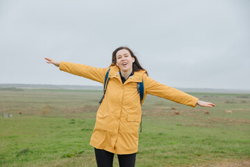 Woman in yellow raincoat keeps arms wide open as if flying. Traveling with a backpack on the North Sea. Traveling in Germany during rain 