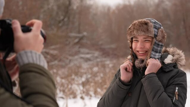 Closeup view slow motion 4k stock video footage of bearded professional photographer taking cute winter pictures of european smiling handsome happy teenage kid at snowy nature background