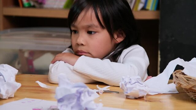 Upset little girl making a colorful drawing at home and crumpled the paper on desk. Girls who are bored with online learning and homework during the coronavirus pandemic.