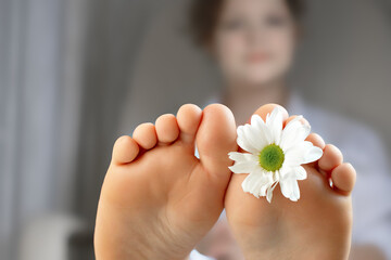 A pair of female bare feet with a chrysanthemum flower between the toes. The concept of healthy skin, massage, pedicure..