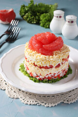 Festive salad with grapefruit, cheese and crab sticks on a white plate on light blue background