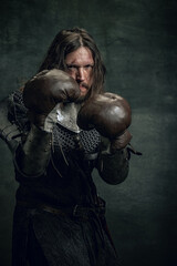 Portrait of medieval warrior or knight with dirty wounded face boxing gloves isolated over dark...