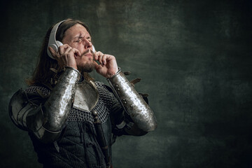 Young medieval warrior or knight with dirty wounded face in headphones listening to music isolated...