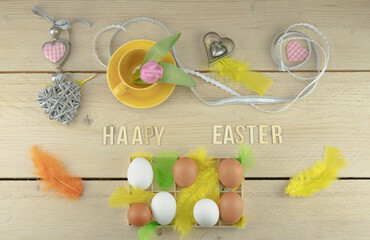 Happy Easter karta, na drewnianym stole ułożone jajka, tulipany, żółte piórka, dekoracja wielkanocna.