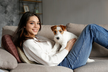 Portrait of young beautiful woman playing with her adorable four months old wire haired Jack Russel terrier puppy. Loving girl with rough coated pup having fun. Background, close up, copy space.