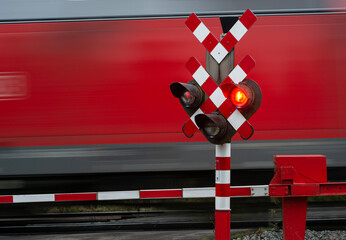Red freight train passes at crossing with red signal and closed barriers. 