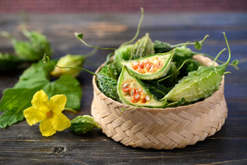 Small bitter gourd or bitter melon in bamboo basket on wooden background, Food ingredients and herbal medicine - obrazy, fototapety, plakaty
