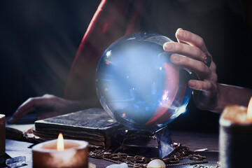 Soothsayer using crystal ball to predict future at table in darkness, closeup. Fortune telling