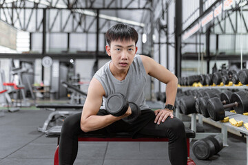 exercise concept The muscular guy in grey sport top and black pants and a black smartwatch working out with the dumbbell by doing concentration curl on his right arm