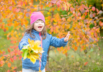 Joyful girl with Downs syndrome throwing autumn leaves at autumn park. Empty space for text