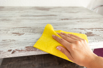 One hand is wiping the surface of a tile with a yellow square shaped cloth and copy space