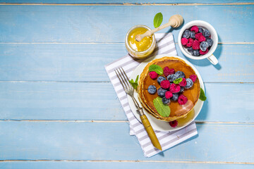Plate of delicious traditional american pancakes with fresh berries and syrup on kitchen table on light background