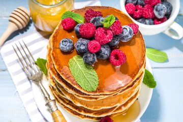Plate of delicious traditional american pancakes with fresh berries and syrup on kitchen table on light background