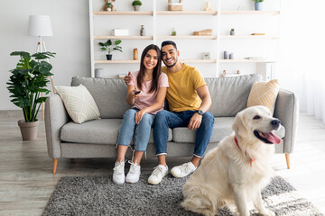 Young loving diverse couple sitting on sofa with dog and watching television, indoors