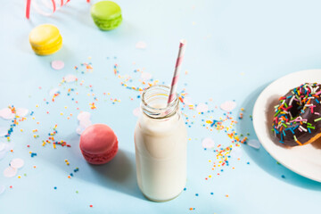 Bottle of milk and delicious donut with chocolate icing with and macaroons on the background. Birthday concept.