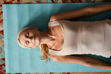 Blonde mature woman lying on mat during yoga practice at home