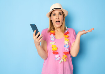 Portrait of young amazed woman wearing jeans and straw hat using smartphone isolated on blue background