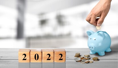 Text of 2022 number written on wooden blocks with blur of coins and pink piggy bank