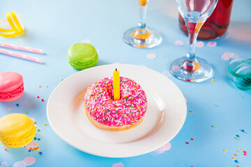 Delicious donut with pink icing and candle bottle of wine, glasses and macaroons on the background. Birthday concept.