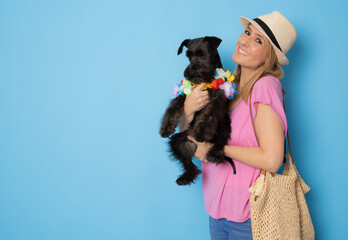Positive female wearing straw hat with glad expression and her dog isolated over blue background. Domestic animals and people.
