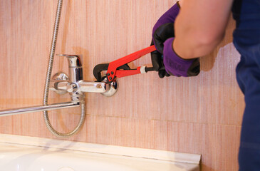 a plumber repairs a faucet in the bathroom. A locksmith in purple gloves.