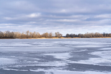 A frozen river covered with snow, a ray of sun falls on an island on the other side of the river