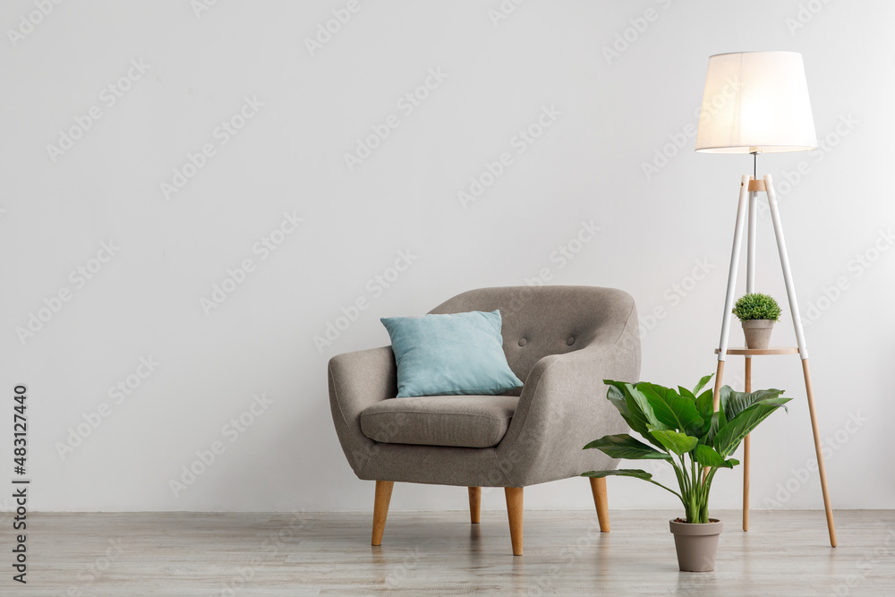 Wall mural comfort armchair with pillow, glowing lamp and potted plant on floor, on gray wall background