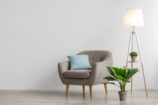 Comfort armchair with pillow, glowing lamp and potted plant on floor, on gray wall background