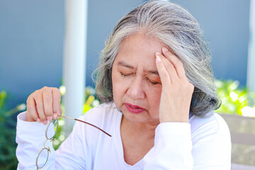 An elderly Asian woman sits and reads a book, she has a headache. Health care concepts, brain...