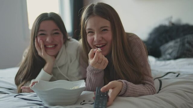 A pajama party with teens eat popcorn on the bed	
