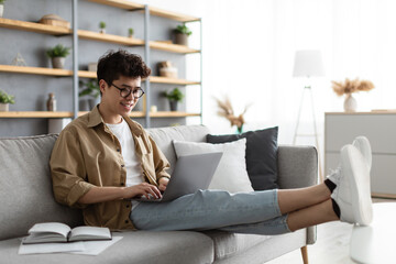 Smiling asian man win glasses orking on laptop at home