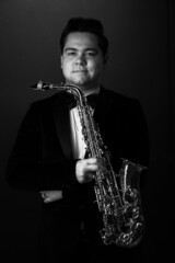 Black and White. Young Saxophonist in a Black Jacket, Hat and Sunglasses Holds a Baritone...