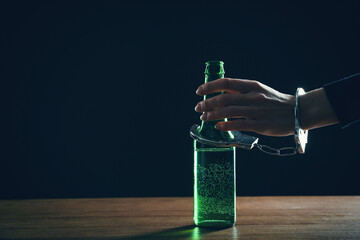 Alcohol addiction. Woman handcuffed to bottle of beer against black background, closeup. Space for text