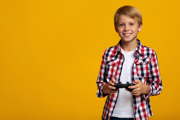 Happy european teenager boy with joystick playing in virtual video game, isolated on yellow background © Prostock-studio