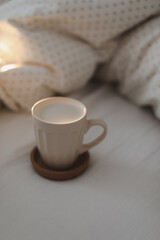 Cup of coffee with milk on the bed with white linens and blanket. Morning coffee in bed concept.