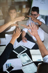 Succeeding is this team's top priority. Shot of a group of coworkers with their hands in a huddle while sitting together around a table in an office.