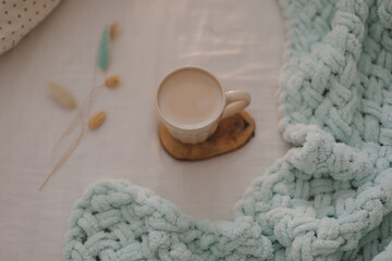 Obraz na płótnie Canvas Cup of coffee with milk on the bed with white linens and blanket. Morning coffee in bed concept.