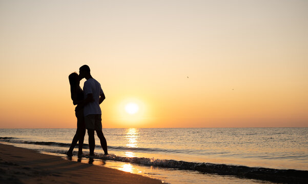 A couple in love is experiencing romantic tender moments at sunset on the beach. Young lovers on summer vacation. concept of love or honeymoon. Kiss in silhouette at sunset.