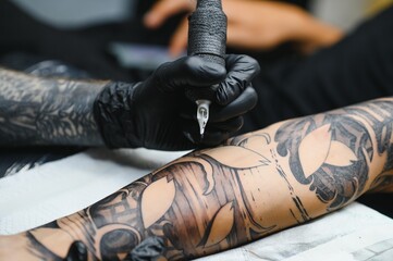 Cropped close up of a bearded tattoo artist working at his studio tattooing sleeve on the arm of his male client. Man getting tattooed by professional tattooist - Powered by Adobe