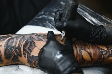 Tattoo artist tattooing a sleeve on a client's arm in a professional studio