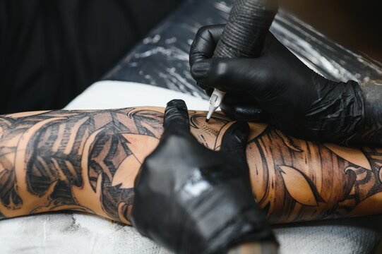 Tattoo salon. The tattoo master is tattooing a man. Tattoo machine, safety and hygiene at work. Close-up, tinted, tattooist.