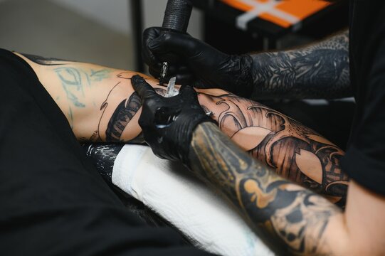 tattooist with his machine tattooing on the arm with the design drawn, concept of art and design