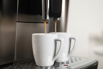 Espresso machine pouring coffee into cups against blurred background, closeup