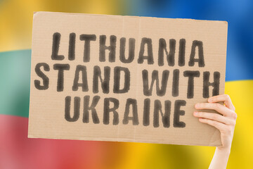 The phrase " Lithuania stand with Ukraine " on a banner in men's hand with blurred Lithuanian and Ukrainian flag on the background. Team. European. War. Assistance. Negotiation. Safety. Security