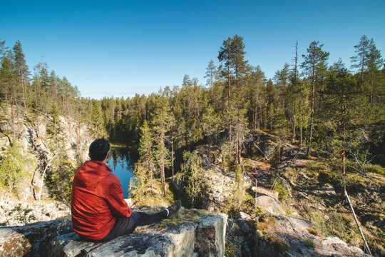 traveller sits on a high rock and observes a beautiful natural lake in hiidenportti national park, Sotkamo in kainuu region, Finland. Hiking the Finnish countryside