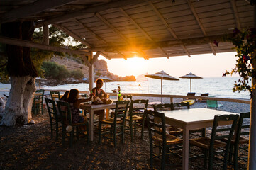 Family enjoying dinner in a restaurant on the beach at sunset.