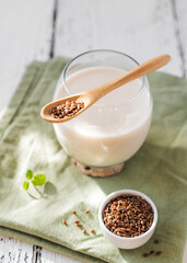 Flaxseed milk in glass with wooden teaspoon on light green napkin, flax seeds, mint leaf. 