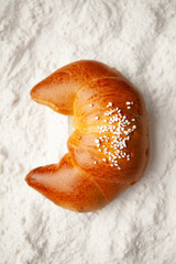 Half-moon bun on white flour background. Sweet homemade cake.