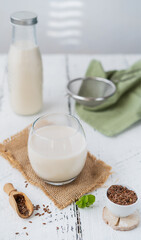 Flaxseed milk in glass on sackcloth, milk bottle, flax seeds, mint leaf, sieve