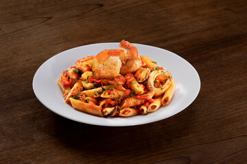 Penne pasta with tomato sauce in white plate on wooden background table. Italian food.